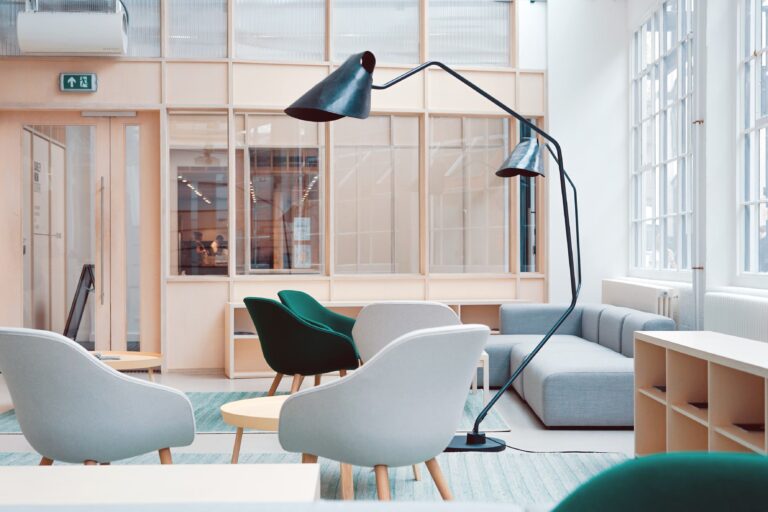 Espace lounge aux tons doux avec fauteuils arrondis, canapé d’angle et grandes lampes noires dans une pièce lumineuse.