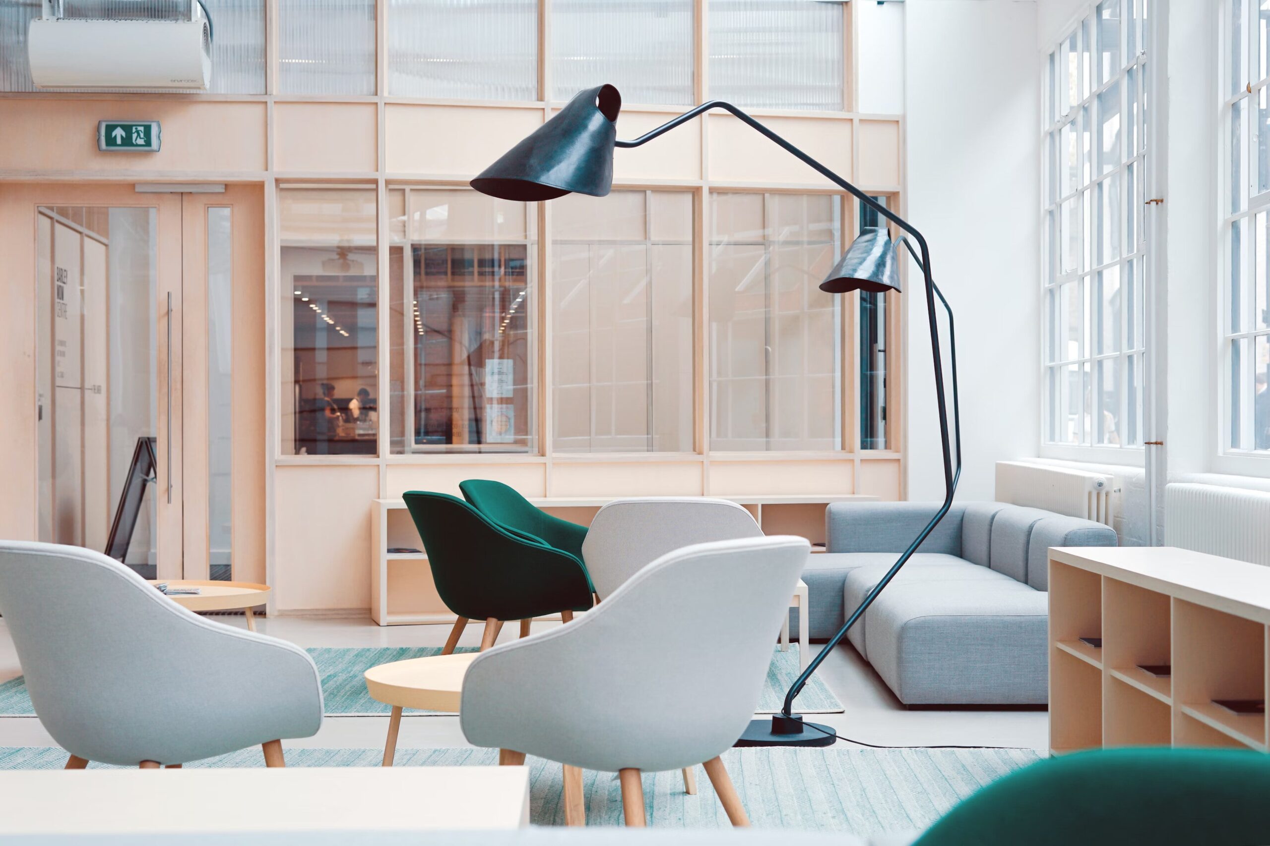 Espace lounge aux tons doux avec fauteuils arrondis, canapé d’angle et grandes lampes noires dans une pièce lumineuse.