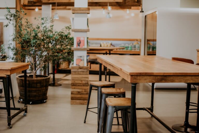 Tables en bois épais avec tabourets métalliques dans un espace de coworking décoré de plantes et d’éléments rustiques
