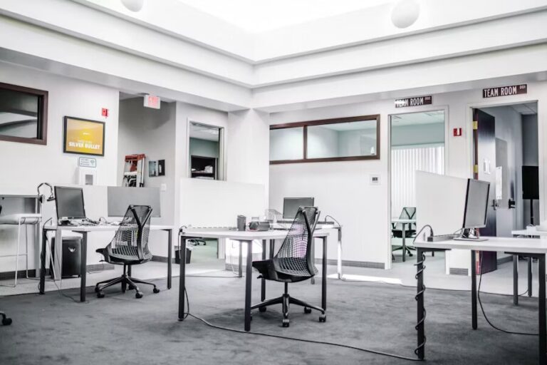 Espace de travail épuré avec mobilier blanc, chaises noires et lumière naturelle dans un style moderne