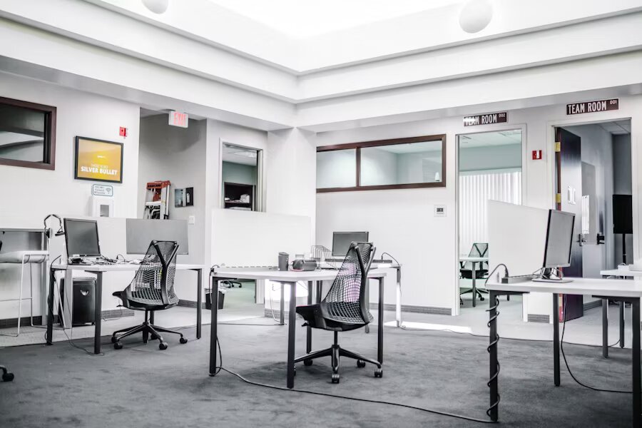 Espace de travail épuré avec mobilier blanc, chaises noires et lumière naturelle dans un style moderne